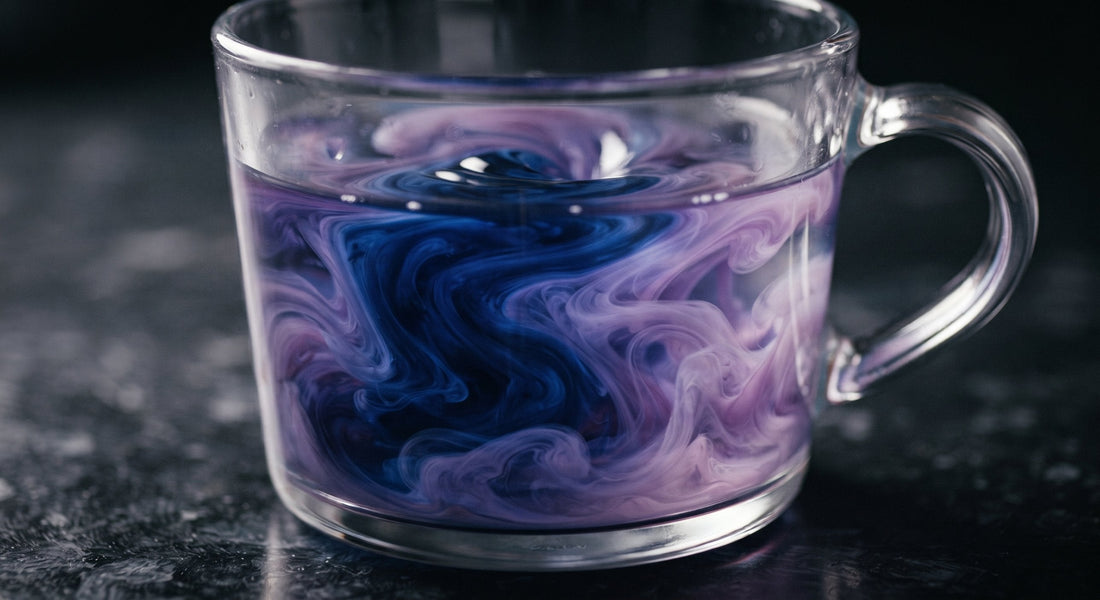Overhead flat-lay of two glass mugs, one deep blue and one mid-shift violet, filled with color-changing mushroom coffee, surrounded by dried mushroom slices, coffee beans, and a bloom sachet on a dark navy background