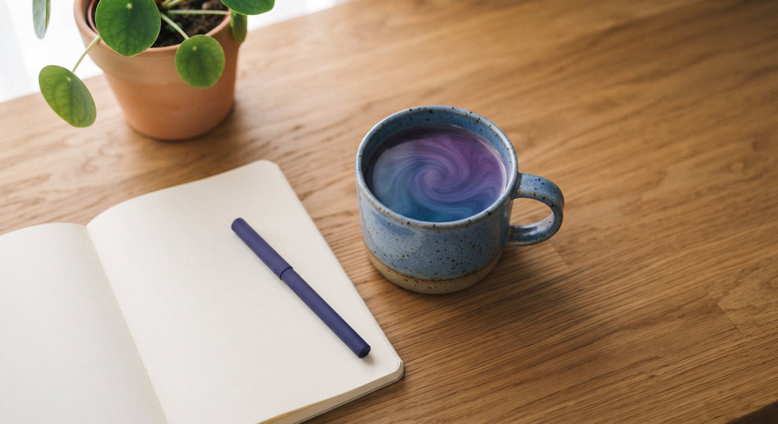 Home office desk with laptop, notebook, potted plant, and a mug of indigo-to-violet color-changing functional coffee in window light